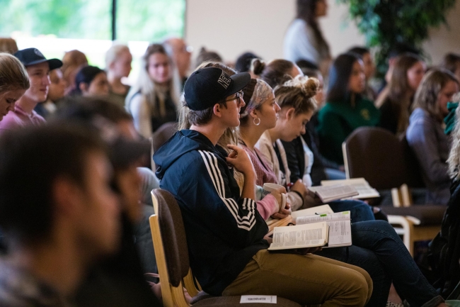 Multnomah University students sit in rows in the campus chapel with books in their laps. 